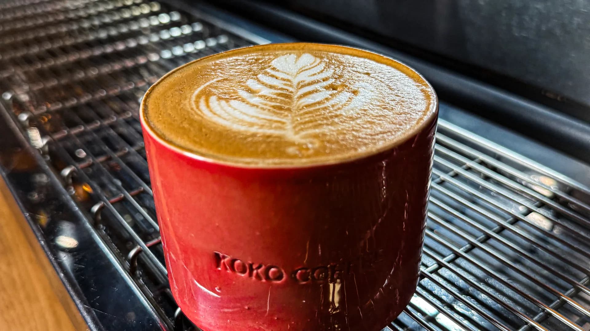 Frisch gebrühter Latte mit Latte Art in roter KOKO-Keramiktasse direkt auf der Siebträgermaschine