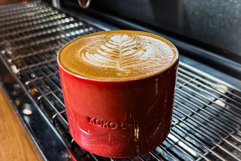 Frisch gebrühter Latte mit Latte Art in roter KOKO-Keramiktasse direkt auf der Siebträgermaschine
