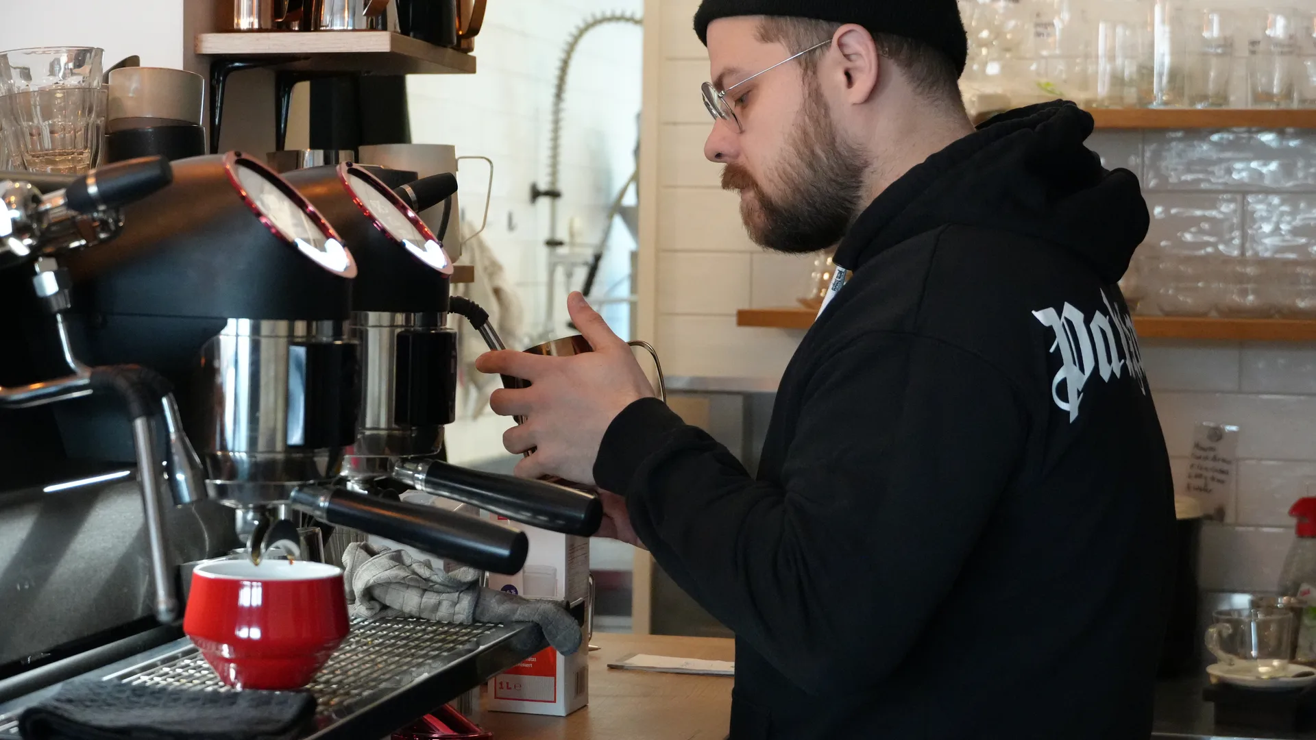 Barista schäumt Milch an der Espressomaschine im KOKO Coffee Lab Würzburg auf, rote Tasse auf der Theke