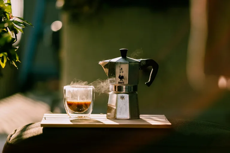 Mokkakanne auf Holztablett mit Espresso-Tasse, warmes Sonnenlicht
