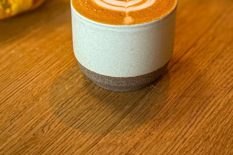 Latte in heller Keramiktasse mit Latte Art, daneben orangefarbene Herbstblumen und Kürbis-Dekoration