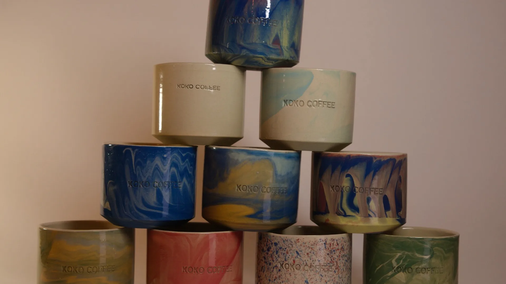 Zehn handgemachte KOKO COFFEE Keramiktassen pyramidenförmig gestapelt in unterschiedlichen Glasuren – blau, grün, rot, weiß mit Farbsprenkeln – Studio-Aufnahme