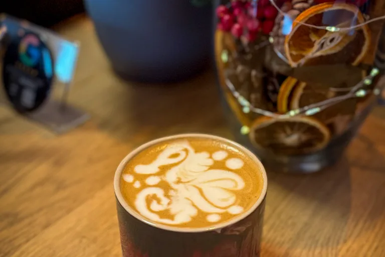 Kunstvolle Latte Art in Form eines Oktopus auf Latte in dunkler Keramiktasse mit Blumen im Hintergrund