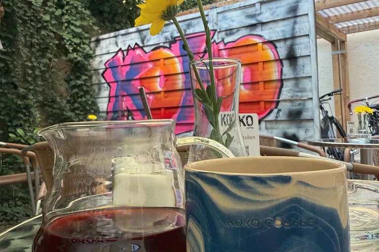 Outdoor-Tisch im KOKO Coffee Lab mit Pour-Over-Karaffe und blauer Keramiktasse, KOKO-Graffiti an der Wand