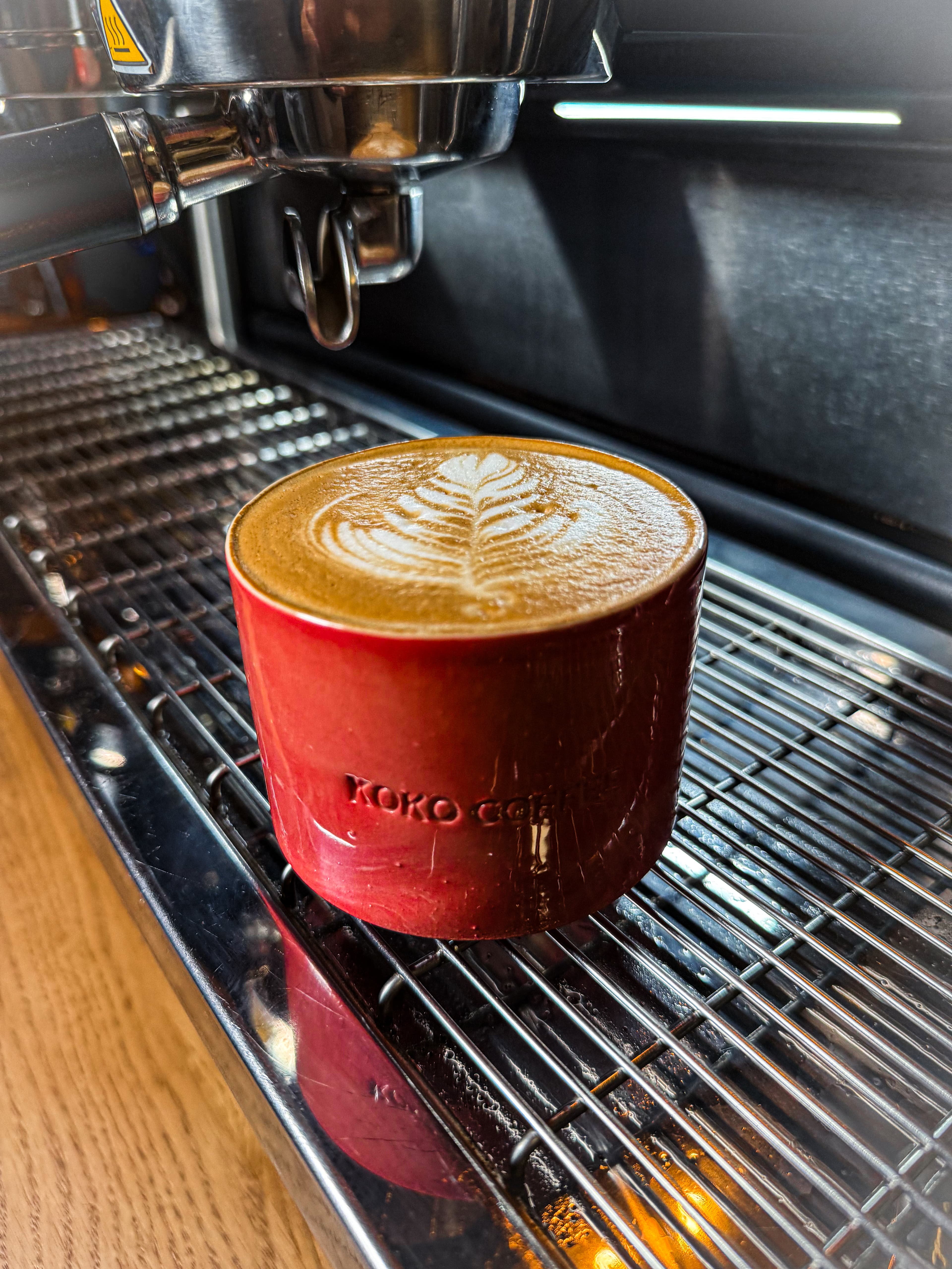 Frisch gebrühter Latte mit Latte Art in roter KOKO-Keramiktasse direkt auf der Siebträgermaschine